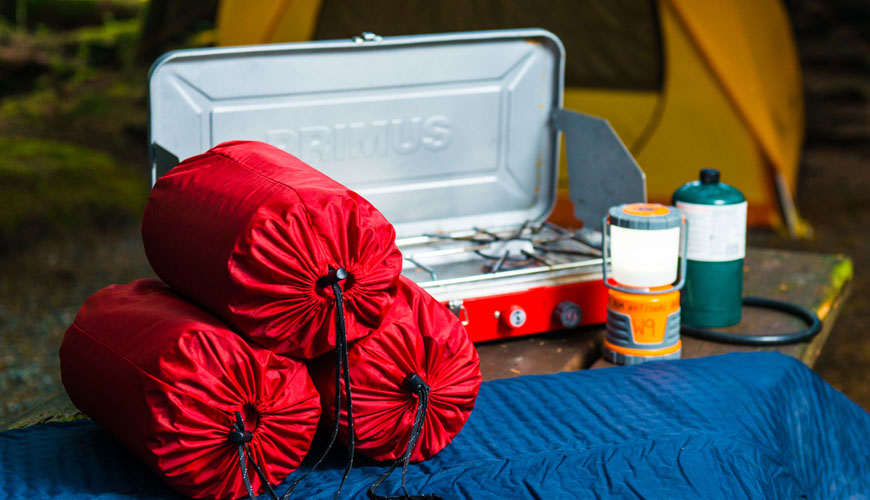 Sacs de couchage, matelas de sol, réchaud de camping, lanterne et tente sur un site de camping.