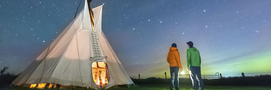 Two visitors gaze at the Big Dipper outside a tipi on a starry night.