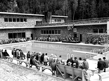Large crowd of people sitting on benches surrounding all for sides of the cool pool at Radium. A speaker is addressing them from a stage