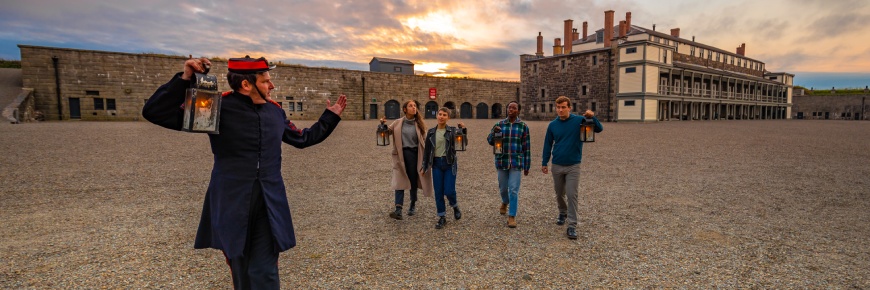 Un guide et quatre adultes se déplacent dans la cour intérieure de la citadelle d’Halifax avec des lanternes.