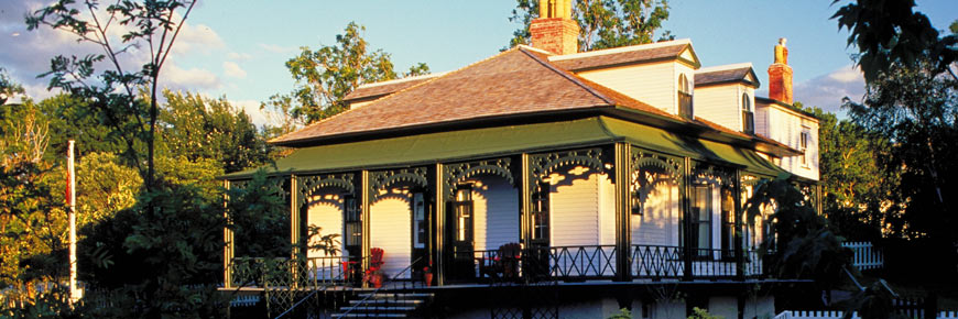A cottage from 1830, with a veranda, surrounded by historic gardens.