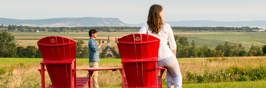 A couple next to red chairs in front of the Grand-Pré landscape