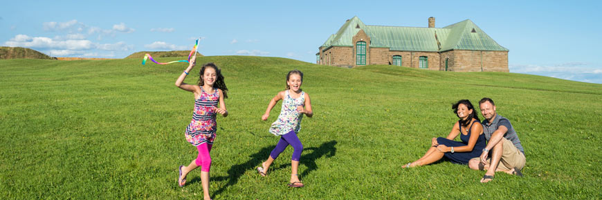 Deux jeunes filles, sous le regard de leurs parents, courent sur un vaste terrain gazonné.