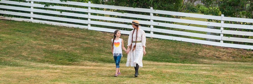 A guide in an Anne Shirley costume with a young girl walk past a historic house. 