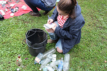 A volunteer takes notes as she kneels in front of a bucket.