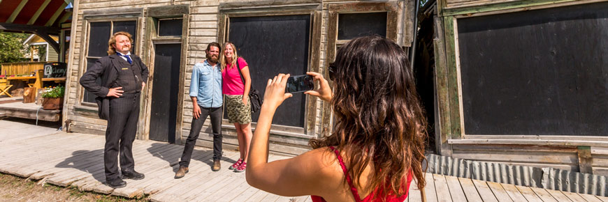 Des adultes se font prendre en photo avec un guide en costume d’époque devant un bâtiment historique.