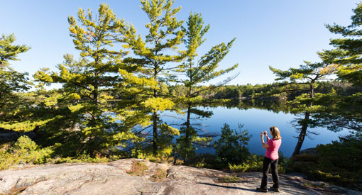A woman stands on a rocky outcrop and takes a picture of the landscape along the Fairy Trail.