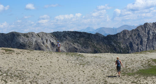 Two visitors hike in the mountains on a rocky ridge.