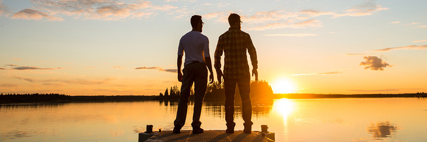 Two visitors stand on the dock and watch the sunset over Astotin Lake, Elk Island National Park