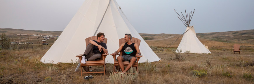 Two men are seated in front of a tipi.