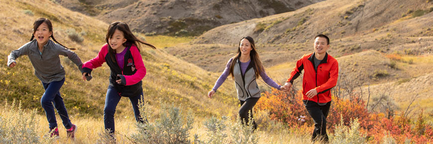 Deux enfants montent une colline en courant, suivis de leurs parents, avec le paysage du bloc Ouest du parc national des Prairies en arrière-plan.