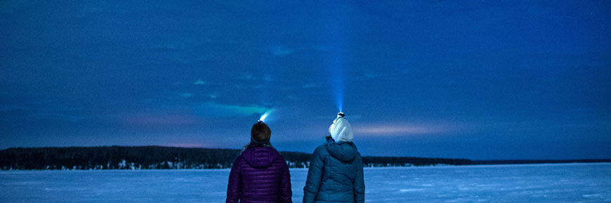 Two visitors gaze at the night sky at the edge of a frozen lake.