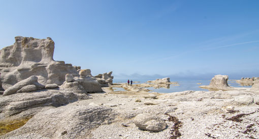 Une vue rapprochée du Château, un groupe de monolithes de la Grande île avec au loin deux visiteurs marchant sur la rive. 
