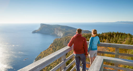 Un jeune couple est en haut de la tour d'observation du mont St-Alban, à 283 mètres d’altitude regardant le paysage de mer, de forêt et de falaises.