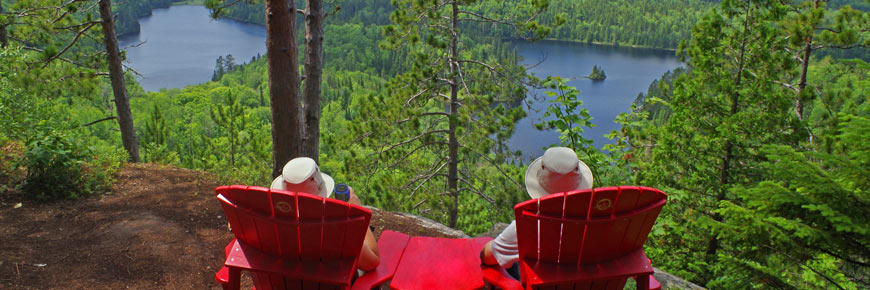 Two visitors rest on the red chairs enjoying the forest landscape.