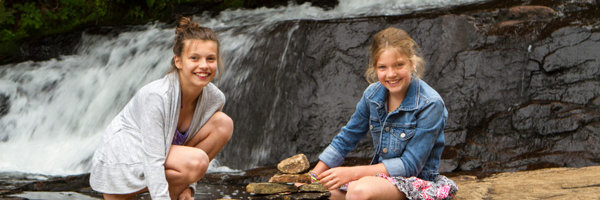 Two young girls are sitting next to the waterfalls.