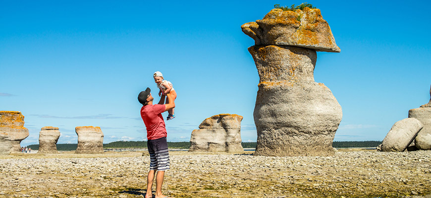 A father and baby playing in front of the limestone monoliths at Anse des Érosions on Île Quarry. Mingan