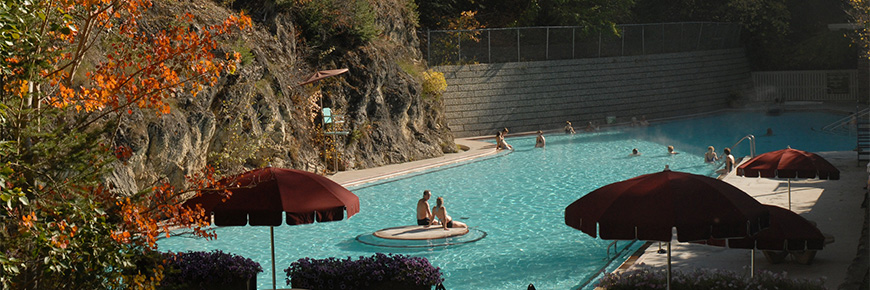 A wide angle view of Radium Hot Springs’ hot soaking pool in autumn.  Nestled inside a cove with Sinclair Canyon`s rock face towering over on the left side of the pool.