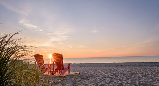 Deux chaises rouges de Parcs Canada sur la plage pendant le coucher du soleil