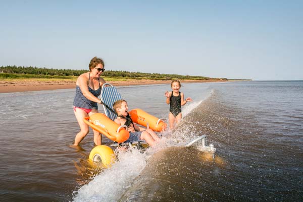 Une famille présentant des besoins en matière d’accessibilité nage dans l’océan en prenant place sur un fauteuil roulant à la plage Stanhope.