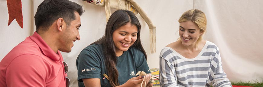 Interprète de Parcs Canada montrant des artefacts autochtones à des visiteurs dans le cadre du programme d’ateliers culturels Anishinabe. Parc national du Mont-Riding.
