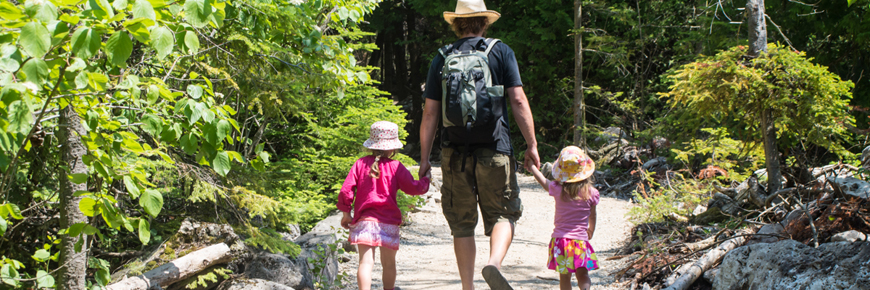 A father holds hands with his children along a trail. 