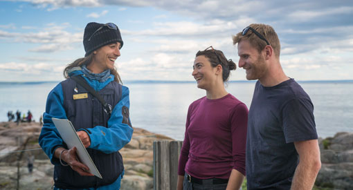 Deux visiteurs discutent avec un guide-interprète sur la rive de l'estuaire du Saint-Laurent. 