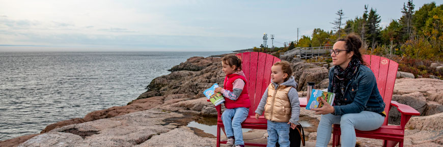 A woman and two children sit on two red chairs and look at the landscape.