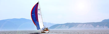 A sailboat with a red and blue sail is sailing in the St. Lawrence estuary.