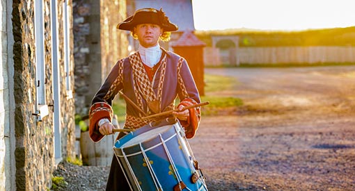 A costumed interpreter dressed as a soldier plays the drums in the lower town area of the Fortress of Louisbourg National Historic Site