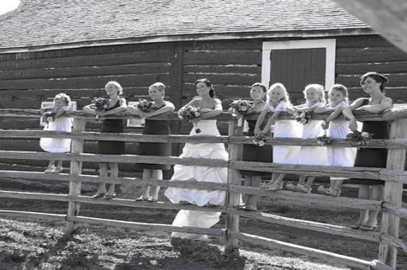 Bride and flower girls stand on a fence at the round pen