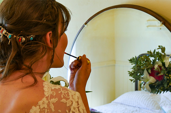 A bride puts on lipstick at a mirror