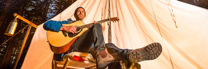 man playing a guitar in front of a tent at night