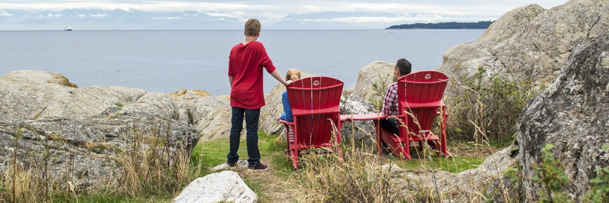A mother, with her son by at her side, and a dad sitting in the red chairs overlooking the Strait of Juan de Fuca and the Olympic Mountain range of Washington State, USA