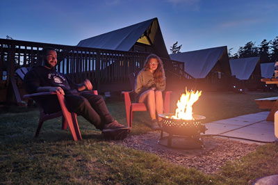 A couple is relaxing by a propane fire pit as the sun sets.