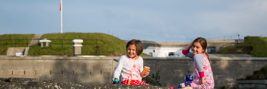 Two children having a picnic on a rock in the Historic Field, with the Lower Battery in the background.
