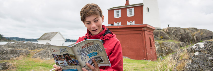 Un garçon lit un livret des Xplorateurs, assis à l’extérieur du phare de Fisgard.