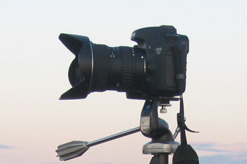 An SLR camera set up on a  tripod near the water.