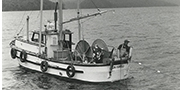 Still frame from vintage black and white film featuring a person fishing from a boat with islands in background