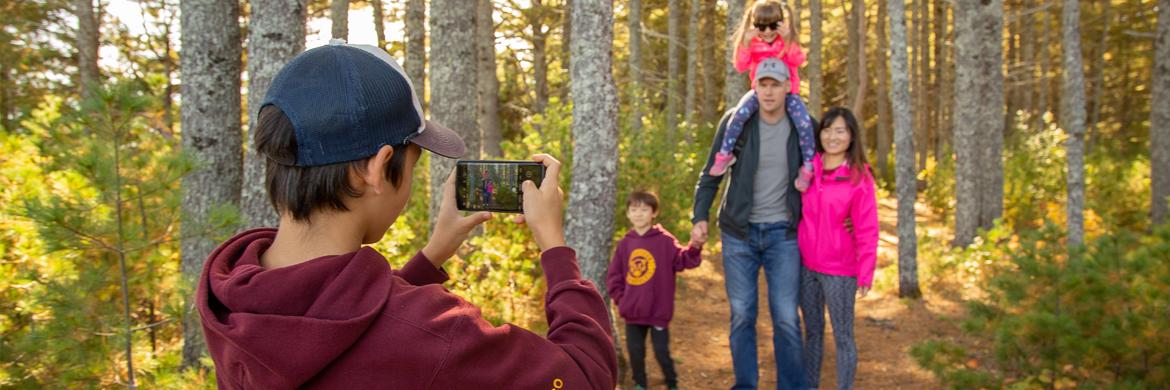 A teenager takes a photo of his family in a trail in the forest.