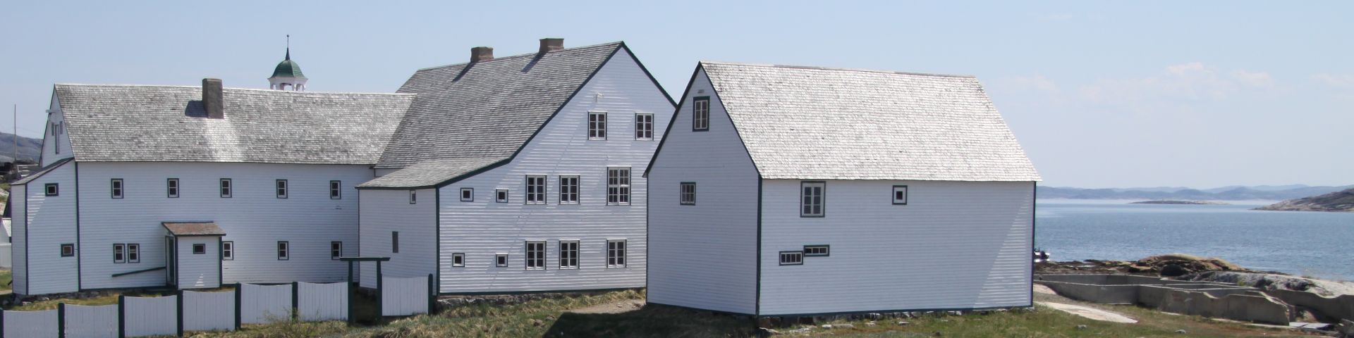 A group of visitors walk between two large wooden buildings at the Hopedale Mission National Historic Site