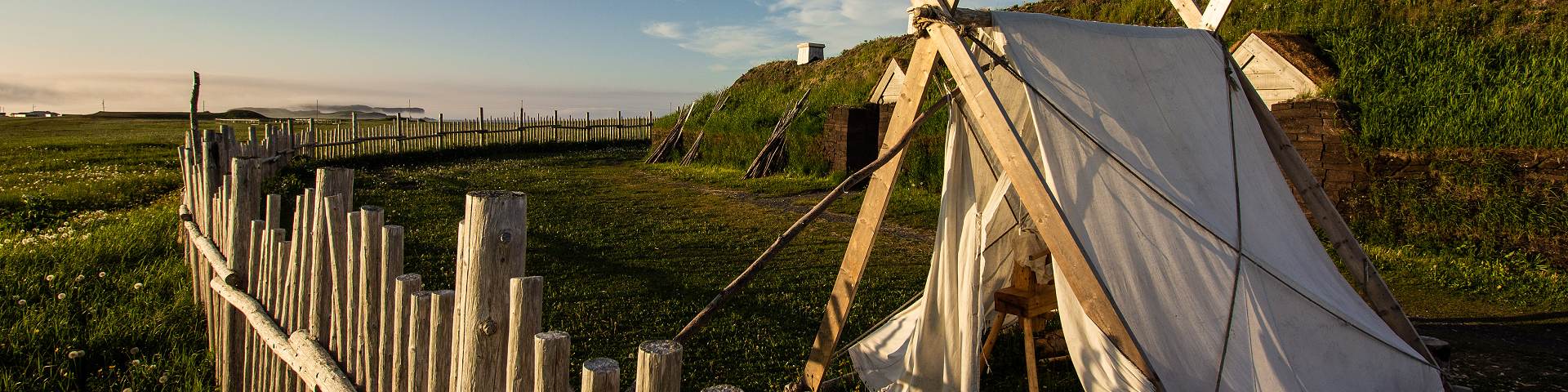 Vue d'une tente en toile devant un bâtiment en bois recouverts de gazon du campement viking au lieu historique national de L'Anse aux Meadows