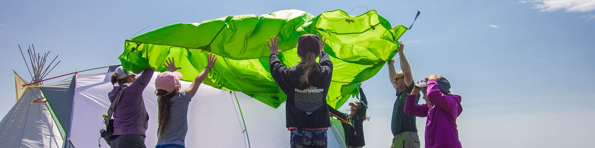 Une personne en uniforme de Parcs Canada monte une tente avec un groupe de jeunes visiteurs au lieu historique national de Port au Choix