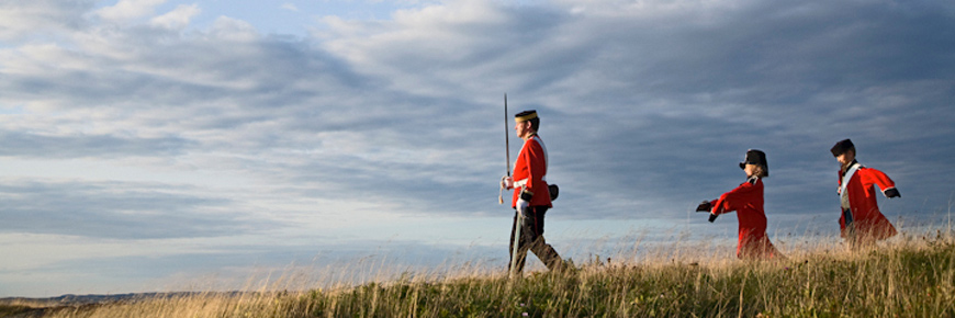Un adulte et deux enfants en uniforme militaire historique marchent sur une colline herbeuse.