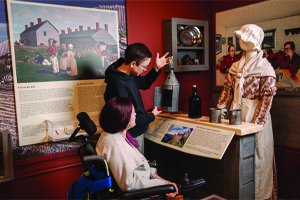 Deux personnes, dont une en fauteuil roulant, explorent l'exposition.