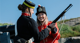 a woman in historic costume teaching how to use a historic rifle