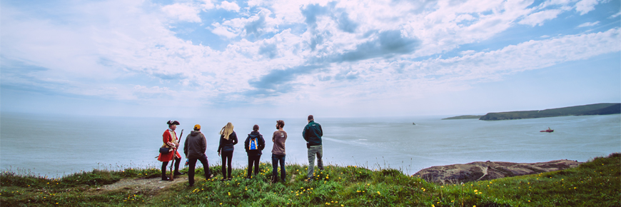 6 people standing on a grassy cliff overlooking the ocean