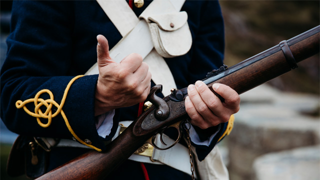 two individuals in historic military uniform holding a historic musket.