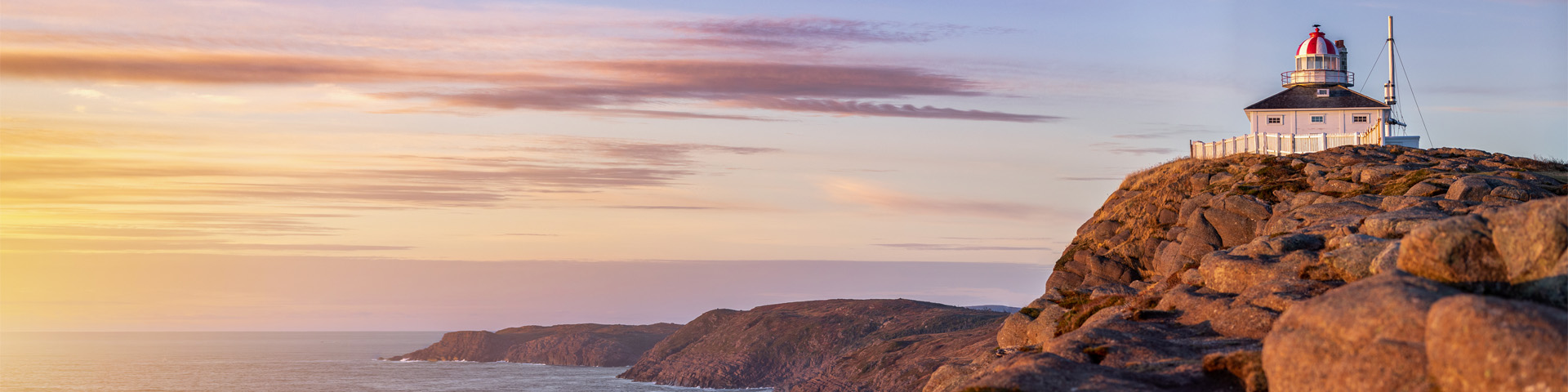 un phare blanc, carré, sur une falaise rocheuse surplombant l'océan sous un lever de soleil coloré