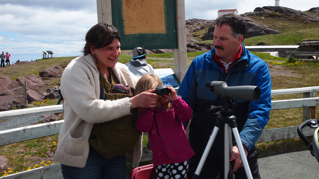 a mother and her child looking through a telescope with the help of another individual
